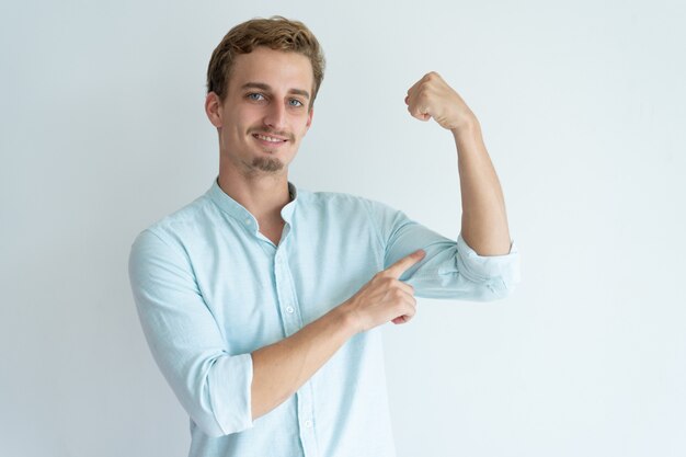 Sonriente joven puño de bombeo y apuntando a bíceps.