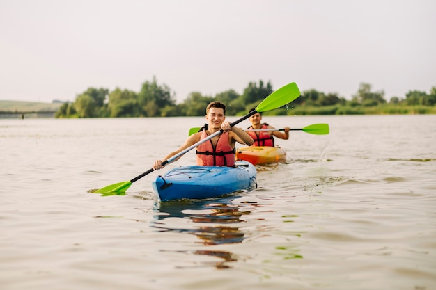 Sonriente joven remando en kayak con su amigo en el lago