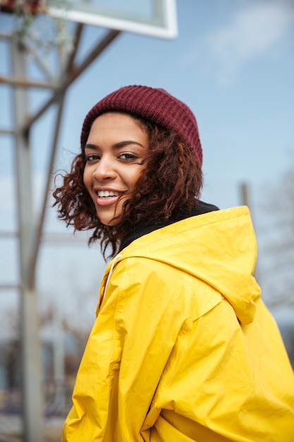 Sonriente joven rizada africana con abrigo amarillo