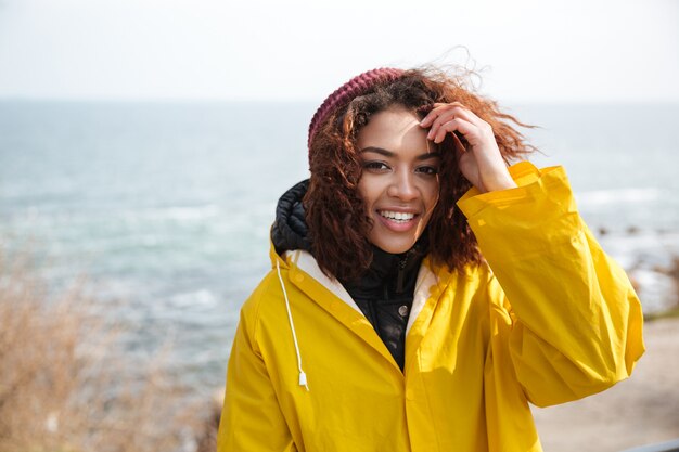 Sonriente joven rizada africana con abrigo amarillo