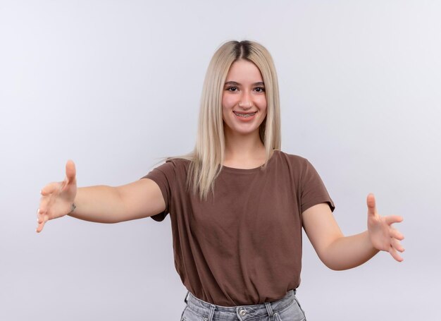 Sonriente joven rubia con aparatos dentales finge sostener algo en un espacio en blanco aislado