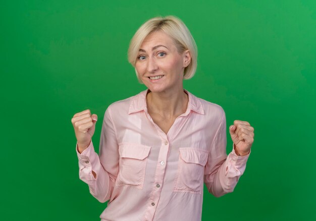 Sonriente joven rubia eslava apretando los puños aislados sobre fondo verde