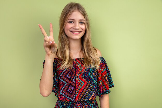 Sonriente joven rubia eslava gesticulando el signo de la victoria mirando al frente