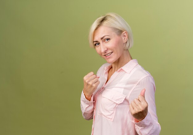 Sonriente joven rubia eslava de pie en pose de lucha aislada en verde oliva