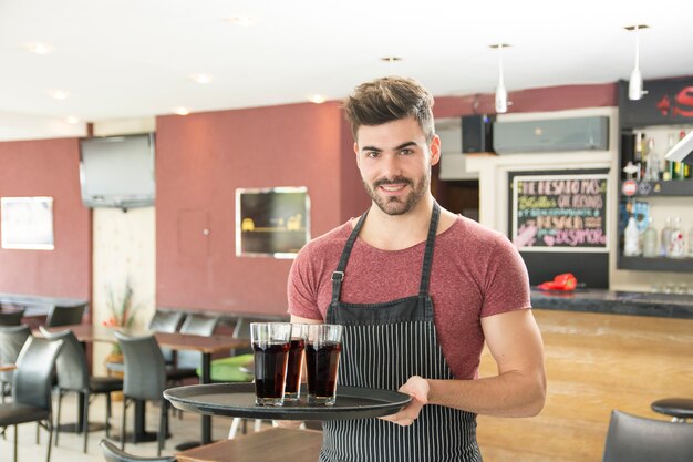 Sonriente joven sirviendo vasos de bebidas en el restaurante