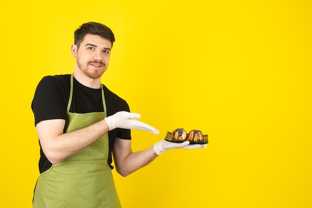 Sonriente joven sobre un amarillo mostrando muffins caseros.