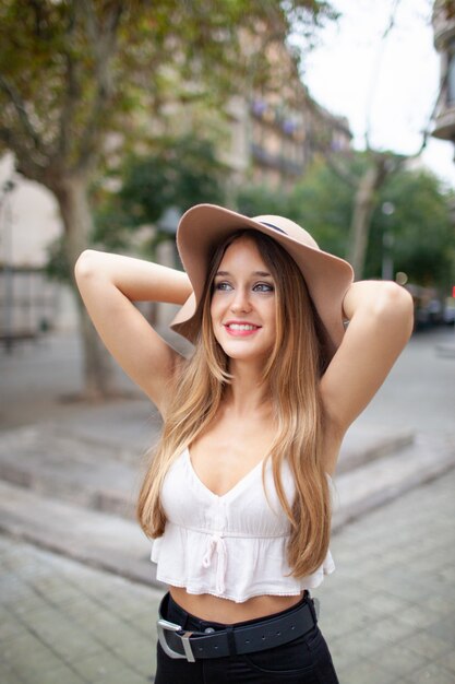 Sonriente joven soñadora con sombrero disfrutando de una visita turística