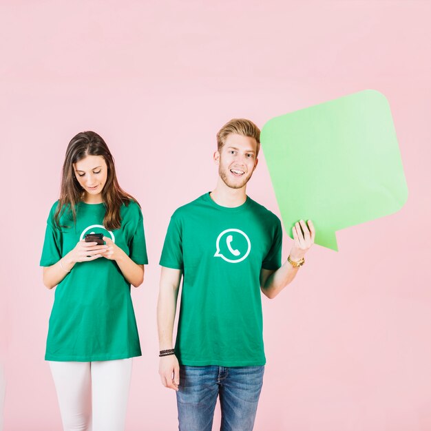 Sonriente joven sosteniendo el bocadillo de diálogo al lado de la mujer que usa el teléfono inteligente