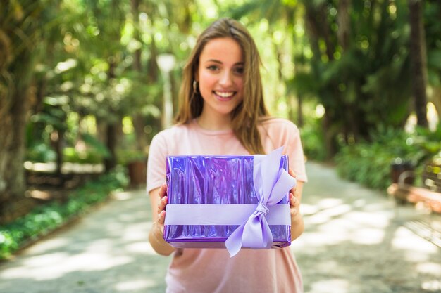 Sonriente joven sosteniendo la caja de regalo púrpura en el parque