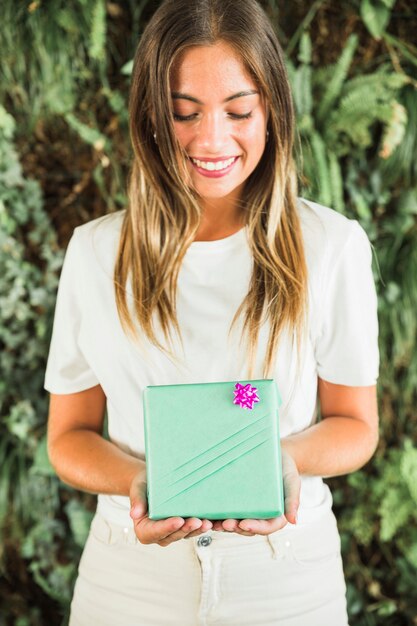 Sonriente joven sosteniendo caja de regalo verde