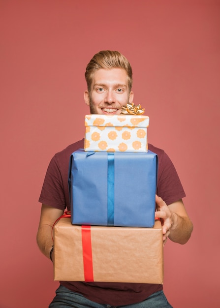 Foto gratuita sonriente joven sosteniendo la pila de cajas de regalo contra el fondo de color