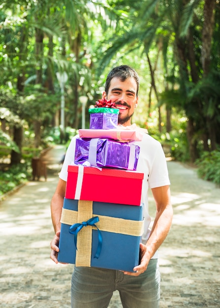 Sonriente joven sosteniendo la pila de regalos en el parque