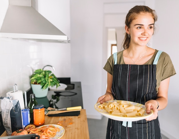 Sonriente joven sosteniendo un plato de pasta en la cocina