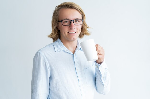 Sonriente joven sosteniendo la taza y mirando a la cámara