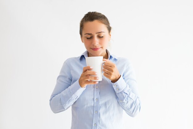 Sonriente joven sosteniendo la taza, oliendo y bebiendo té