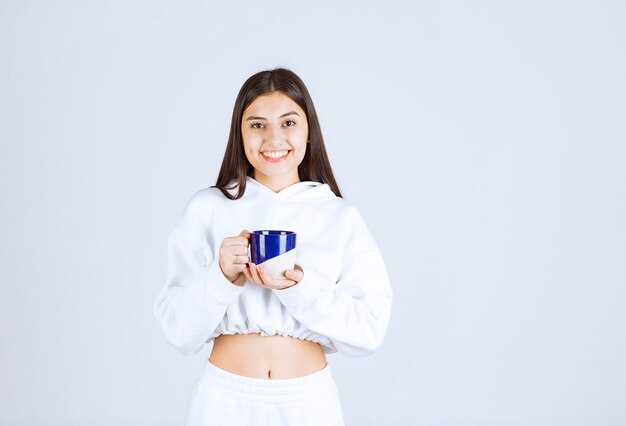 sonriente joven sosteniendo una taza sobre fondo blanco-gris.