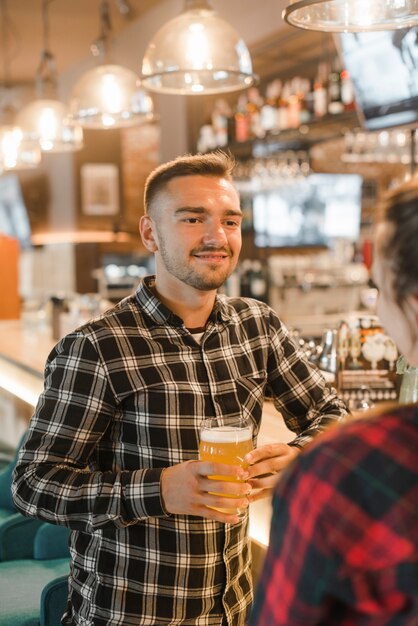 Sonriente joven sosteniendo un vaso de cerveza con su amiga