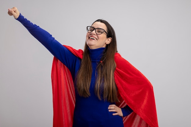 Sonriente joven superhéroe con gafas levantando el puño aislado en blanco