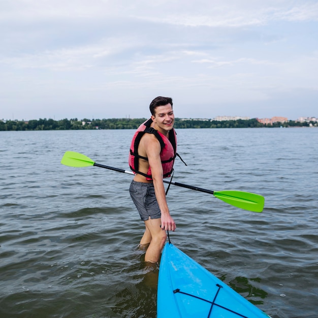 Sonriente joven tirando de kayak en el lago