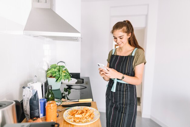 Sonriente joven tomando foto de plato de pasta preparada en teléfono celular