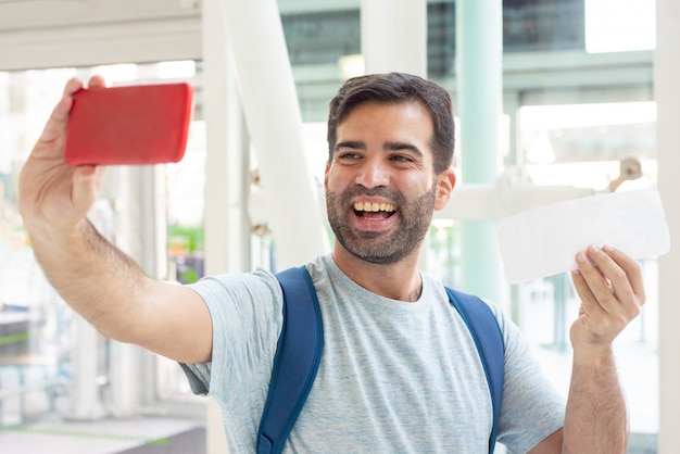 Sonriente joven tomando selfie con boleto