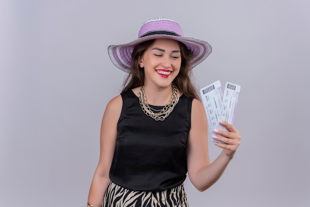 Sonriente joven viajero vistiendo camiseta negra con sombrero sosteniendo boletos sobre fondo blanco.