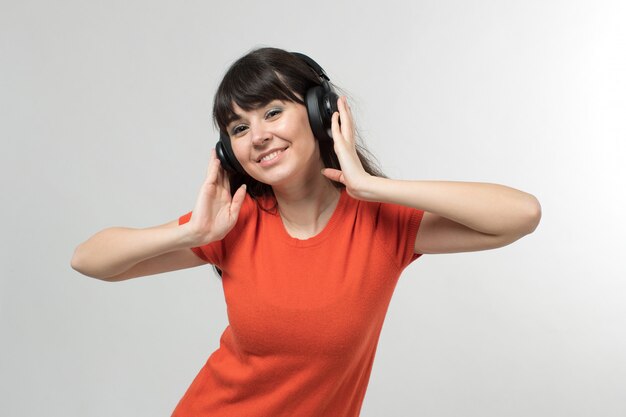 Sonriente jovencita escuchando música a través de auriculares en camiseta diseñada de buen humor con el pelo largo en blanco