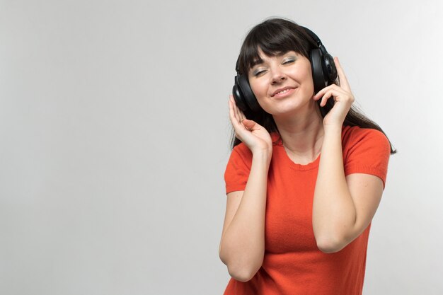 Sonriente jovencita escuchando música a través de auriculares en camiseta diseñada de buen humor con el pelo largo en blanco