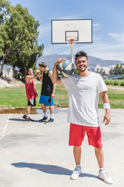 Sonriente jugador de baloncesto sosteniendo la pelota sobre el hombro