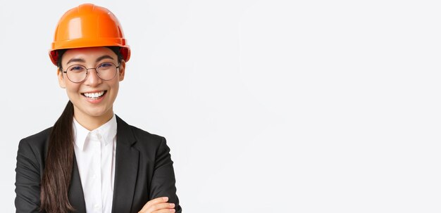 Sonriente líder del equipo ingeniera jefe asiática en casco de seguridad y traje de brazos cruzados con confianza