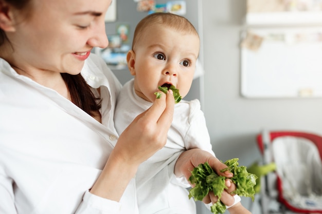 Sonriente linda madre alimentando a bebé con lechuga