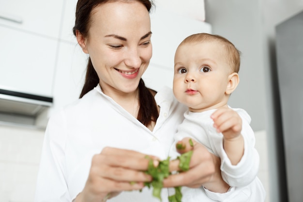 Sonriente linda madre alimentando a bebé con lechuga