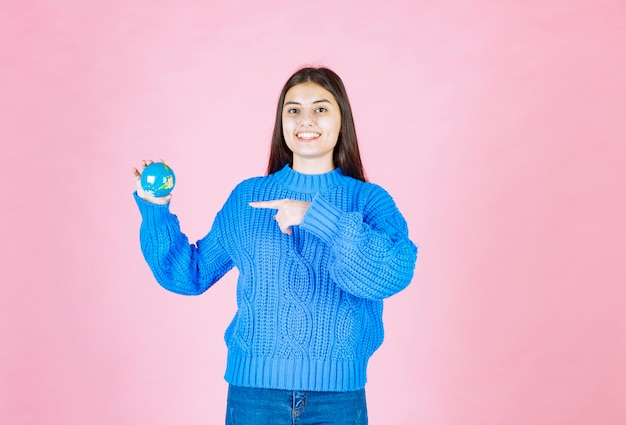 sonriente modelo de niña apuntando a la pequeña bola de la tierra.