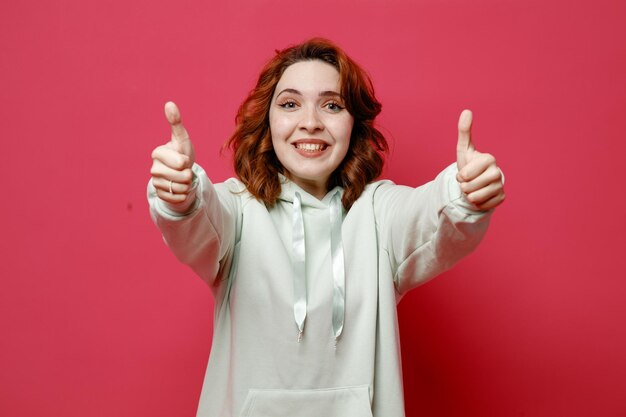 Sonriente mostrando los pulgares hacia arriba joven hermosa chica en suéter blanco aislado sobre fondo de color rosa