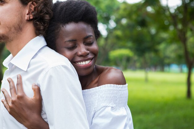 Sonriente mujer abrazando a su hombre con los ojos cerrados