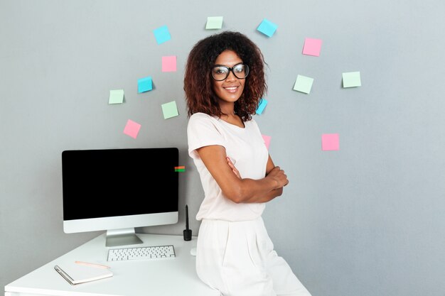 Sonriente mujer africana en anteojos de pie cerca de la mesa