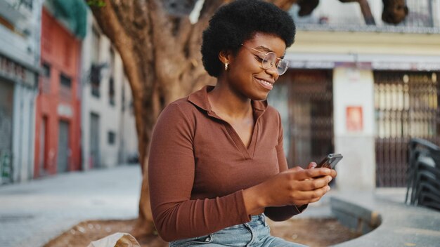 Sonriente mujer africana en ropa casual charlando con amigos por teléfono