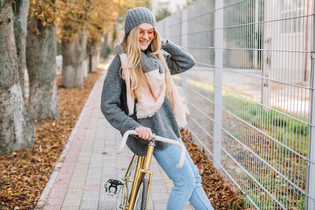 Sonriente mujer apoyándose en bicicleta cerca de la valla