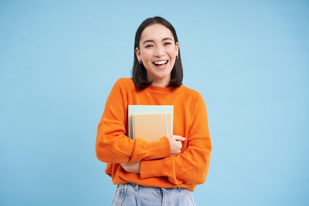 Foto gratuita sonriente mujer asiática con cuadernos estudiante con cara feliz promoción de educación universitaria fondo azul