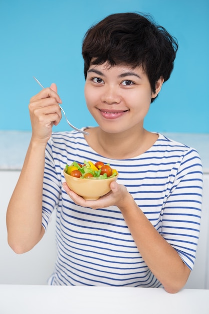 Sonriente mujer asiática joven comiendo ensalada de verduras