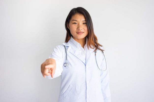 Sonriente mujer asiática médico apuntando a usted.