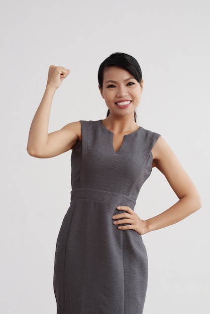 Sonriente mujer asiática en traje de negocios posando en estudio y flexionando su brazo