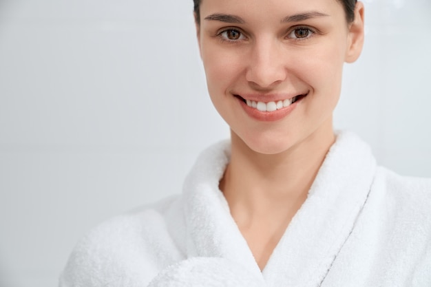 Sonriente mujer atractiva en bata blanca de pie en el baño.
