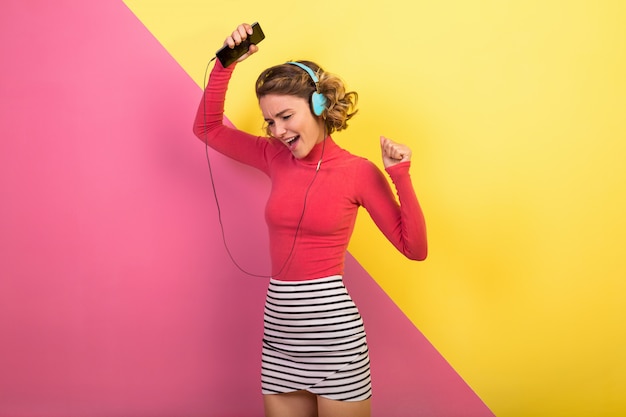 Sonriente mujer atractiva en elegante traje colorido bailando y escuchando música en auriculares