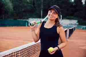 Foto gratuita sonriente mujer atractiva en ropa deportiva, de pie en la cancha con raqueta de tenis