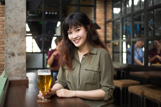 Sonriente mujer bastante asiática bebiendo cerveza en Pub