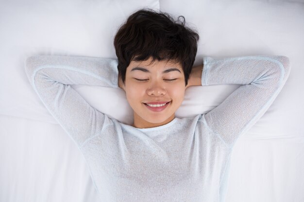 Sonriente mujer bastante asiática durmiendo en la cama