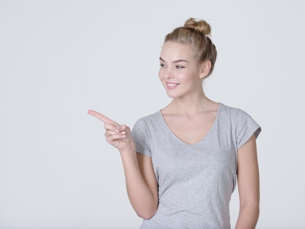 Sonriente mujer bonita apuntando con el dedo sobre fondo gris. Mirando a la camara