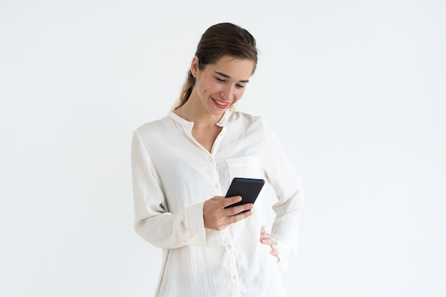 Sonriente mujer bonita joven sosteniendo y usando el teléfono inteligente.