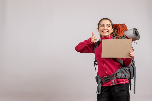 Foto gratuita sonriente mujer bonita con mochila grande sosteniendo cartón dando pulgar hacia arriba